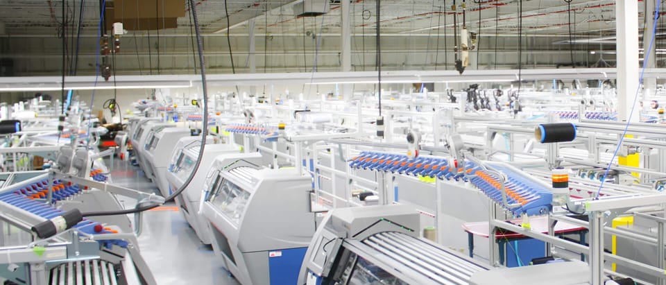 The Mississauga campus interior — the advanced-materials floor and knitting machines in one continuous space, wide and real.