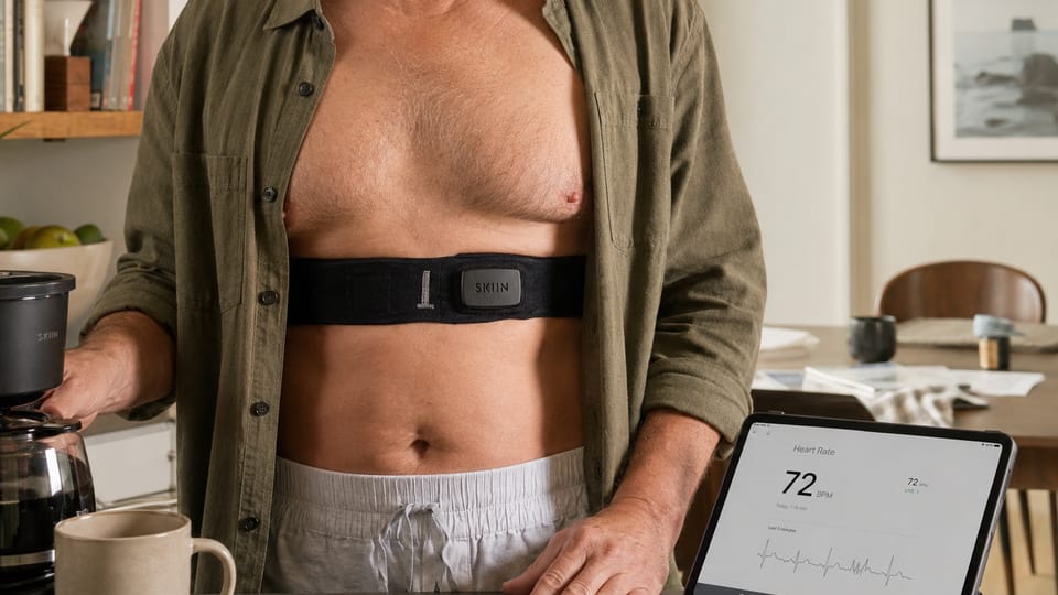 A person at home wearing a SKIIN cardiac band, live heart rate on a tablet beside them